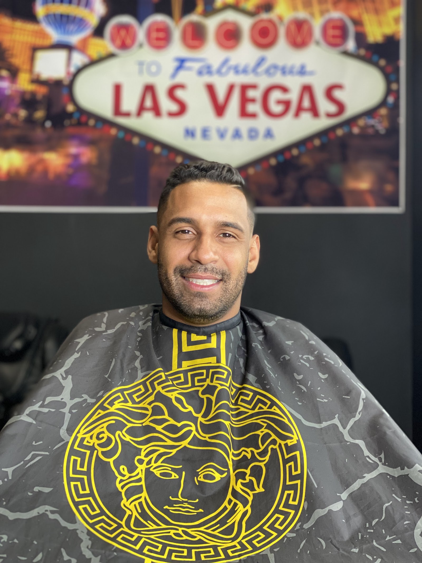Smiling client with a fresh haircut seated in a barber chair under a Las Vegas sign backdrop