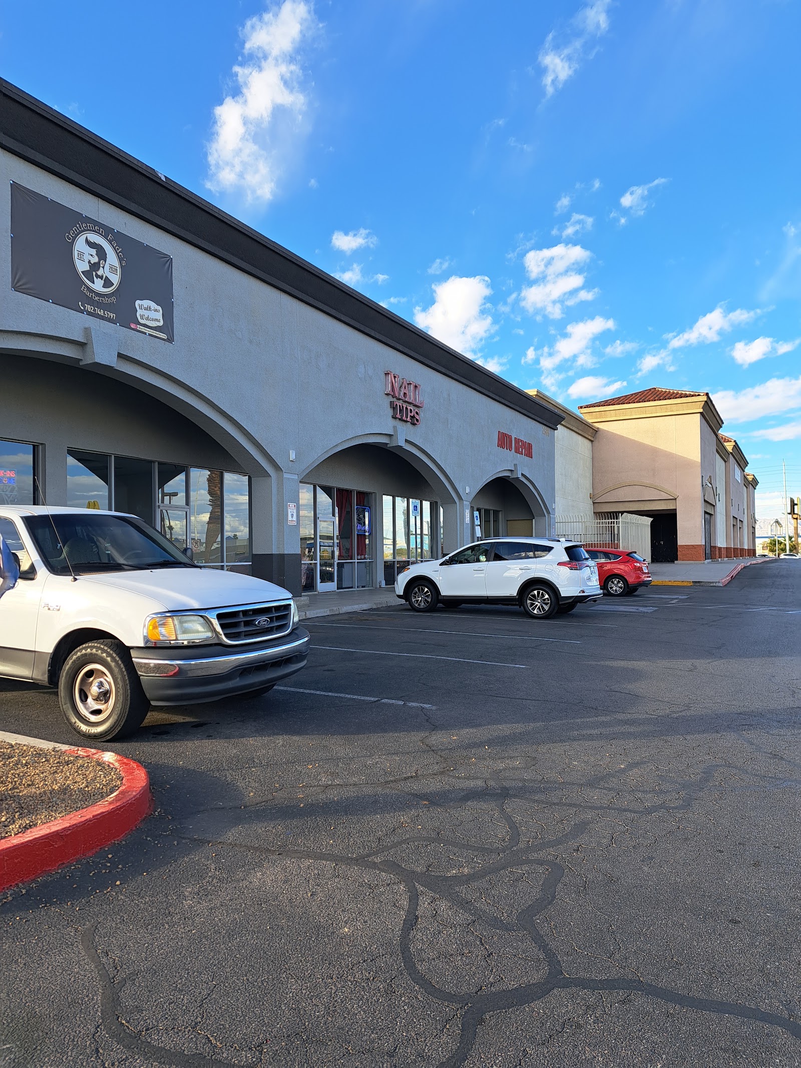 Strip mall exterior showing the barbershop with neighboring nail and auto repair shops